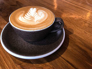 Coffee in gray cup on wooden table in cafe with lighting background