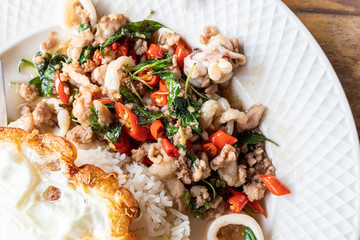 Stir fried squid basil and minced pork with steamed rice and fried egg on a white plate.