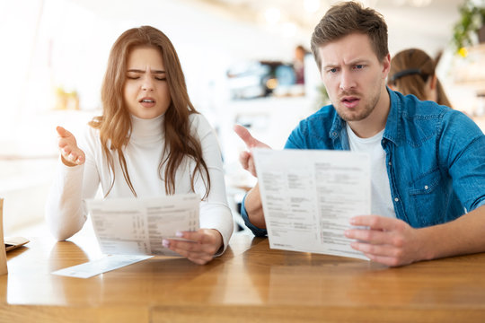 young couple beautiful woman and and her handsome man look unsatisfied holding menu choosing what to order in cafe during lunch time, unhappy guests