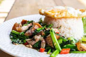 Crispy pork with Chinese kale with steamed rice and fried egg on a white plate.