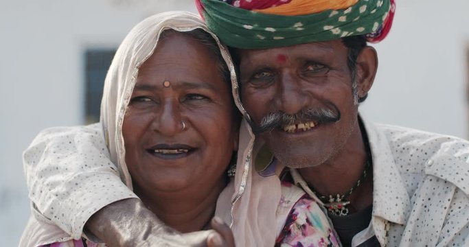 Close-up portrait of a loving positive happy confident Indian elderly rural couple wearing traditional dress in Rajasthan, looking with joy and happiness at camera for photo video with toothy smiles 