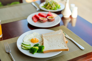 Fresh romantic breakfast table next to window with bread, fruit, juice, milk, egg, vegetable...