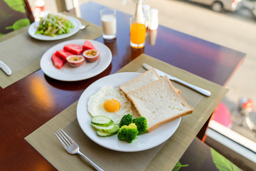 Fresh romantic breakfast table next to window with bread, fruit, juice, milk, egg, vegetable...