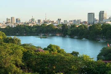 Fototapeta na wymiar Hoan Kiem lake or Sword lake, Ho Guom in Hanoi, Vietnam with Turtle Tower, green trees and buildings on horizon