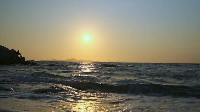 Beautiful yellow sunset over sea with waves splashing on shore.