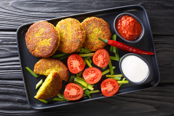 Yellow split pea fritters with fresh vegetables and sauces close-up in a plate. Horizontal top view