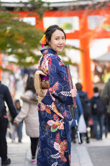 Geishas girl wearing Japanese kimono among red wooden Tori Gate at Fushimi Inari Shrine in Kyoto, Kimono is a Japanese traditional garment. The word "kimono", which actually means a "thing to wear"