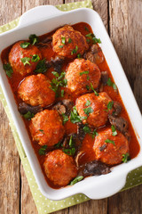 Homemade meatballs with wild mushrooms and tomato sauce close-up in a baking dish. Vertical top view