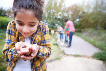 Girl Holding Small Frog As Group Of Children On Outdoor Activity Camp Catch And Study Pond Life - Powered by Adobe