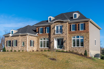 Fototapeta na wymiar Newly constructed American luxury house symmetric facade covered by stone and brick, arched decorative white casement windows sash separated by grills, accent trim, dormer on roof, side vinyl