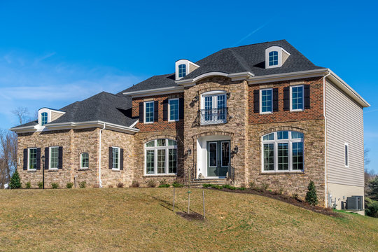 Newly constructed American luxury house symmetric facade covered  by stone and brick, arched decorative white casement windows sash separated by grills, accent trim, dormer on roof, side vinyl