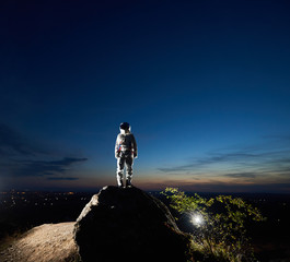 Space traveler standing on rocky hill under beautiful blue sky. Cosmonaut wearing white space suit...