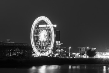Night long exposure ferris wheel moving blur in black and white at a street outdoor festival.