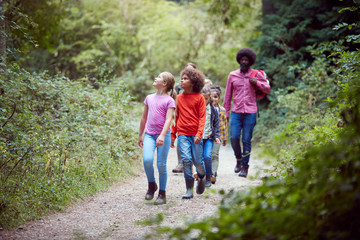 Fototapeta premium Adult Team Leaders With Group Of Children At Outdoor Activity Camp Walking Through Woodland