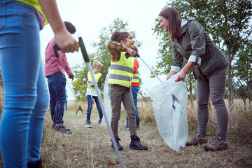 Adult Team Leaders With Group Of Children At Outdoor Activity Camp Collecting Litter Together