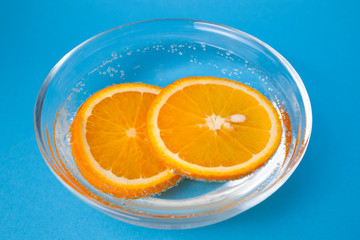 Orange slices in a plate in sparkling water on a blue background.