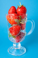 Strawberries in a glass of sparkling water on a blue background.