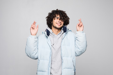 Handsome curly man with head of curly hair standing against white background with crossed fingers...