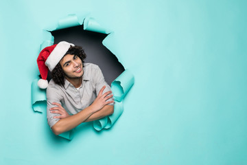 Young curly handsome man wear in santa hat from hole on green paper