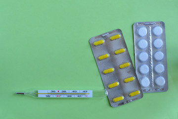 Yellow and white pills in blisters and a thermometer with copy space