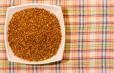 Raw buckwheat in white ceramic bowl on a colored napkin , concept of healthy eating vegan food. Close up, copy space