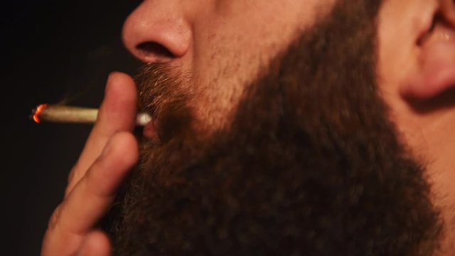 Close up of a man with a beard lighting and smoking a cannabis joint