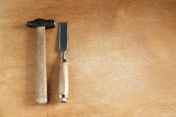 One chisel with a wooden handle and an old hammer with a wooden handle are on the wooden table on the left and the copyspace on the right.