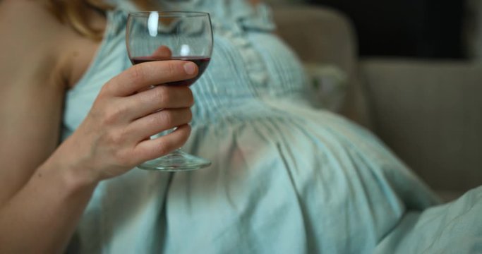 Pregnant woman drinking red wine on the sofa at home
