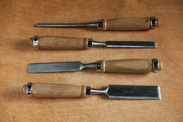 Four wood chisels with wooden handles lie horizontally on each other on a wooden table.