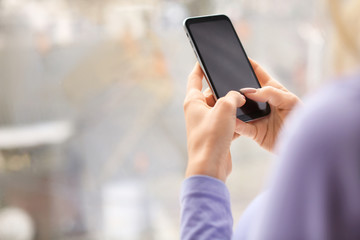 Young woman with mobile phone near window