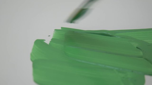 Close up artist painting with acrylic green paint brush on white paper