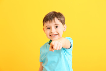 Happy smiling little boy pointing at viewer on color background