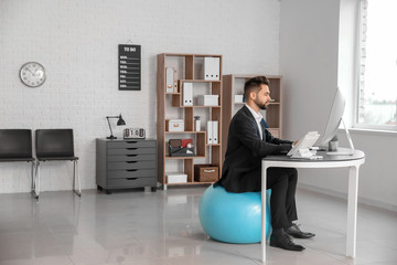 Businessman sitting on fitness ball while working in office