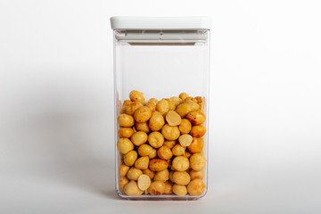 Macadamias inside a transparent plastic container with a white background, also called Queensland, bush, maroochi, bauple and Hawaii nut