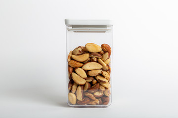 Raw Brazil nuts inside a transparent plastic container with a white background, also called Bertholletia or paranoot