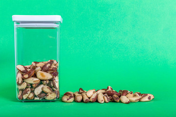 Brazil nuts raw also called bertholletia or paranoot. They are in a transparent plastic container with a green background