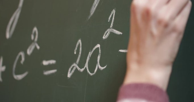 Human hand writing math equation on green chalkboard, closeup