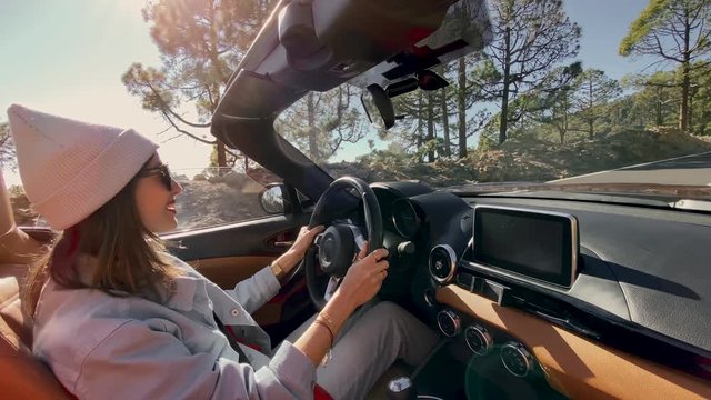 Young stylish woman driving convertible car while travel in the mountain forest. Video recorded on a smartphone