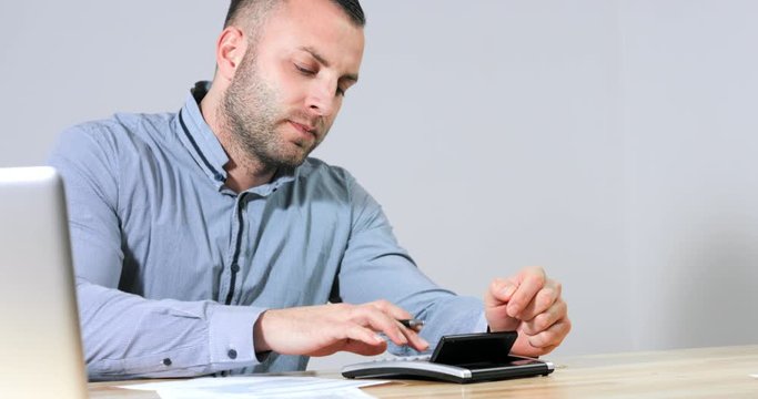 Frustrated businessman under stress nervously filling 1040 tax form with calculator at office desk. 4k footage resolution.
