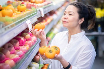Asian beautiful woman shopping for organic fruits at supermarket. healthy lifestyle concept