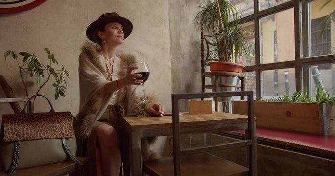 confident strong independent lady girl woman in retro sits in a restaurant with a glass of wine while waiting for someone
