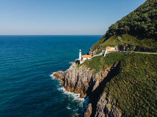 Aerial shot of cliff with lighthouse on the ledge and the ocean hitting the rocks