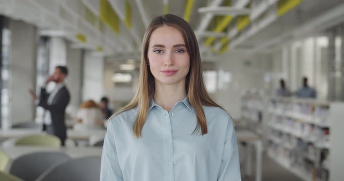 Smiling girl intern standing in modern office space.Portrait of ambitious young woman office worker looking to camera with serious face. Concept of people and career.Blurred background.