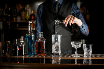 Bartender is preparing alcoholic cocktail with ice in a glass behind the bar.