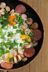 fried sausage and sausages with fried eggs and herbs in a pan top view. hearty hot breakfast