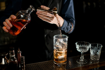Barman measures the ingredients for cocktail from bottle with brown alcohol drink.