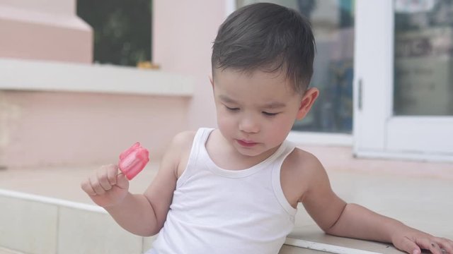 Slow Motion video of Asian child eating and biting on red strawberry ice cream while sitting on the stairs outside of the house