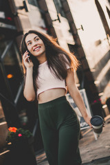 Smiling woman using phone and drink coffee on the street in summer day.
