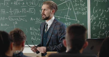 Confident middle aged teacher explaining material to schoolchildren in classroom, math lesson