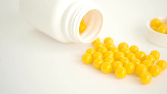 Vitamins. Antiviral drug tablets. Round yellow healthy pills and pill bottle on white background. Slow motion. Close-up